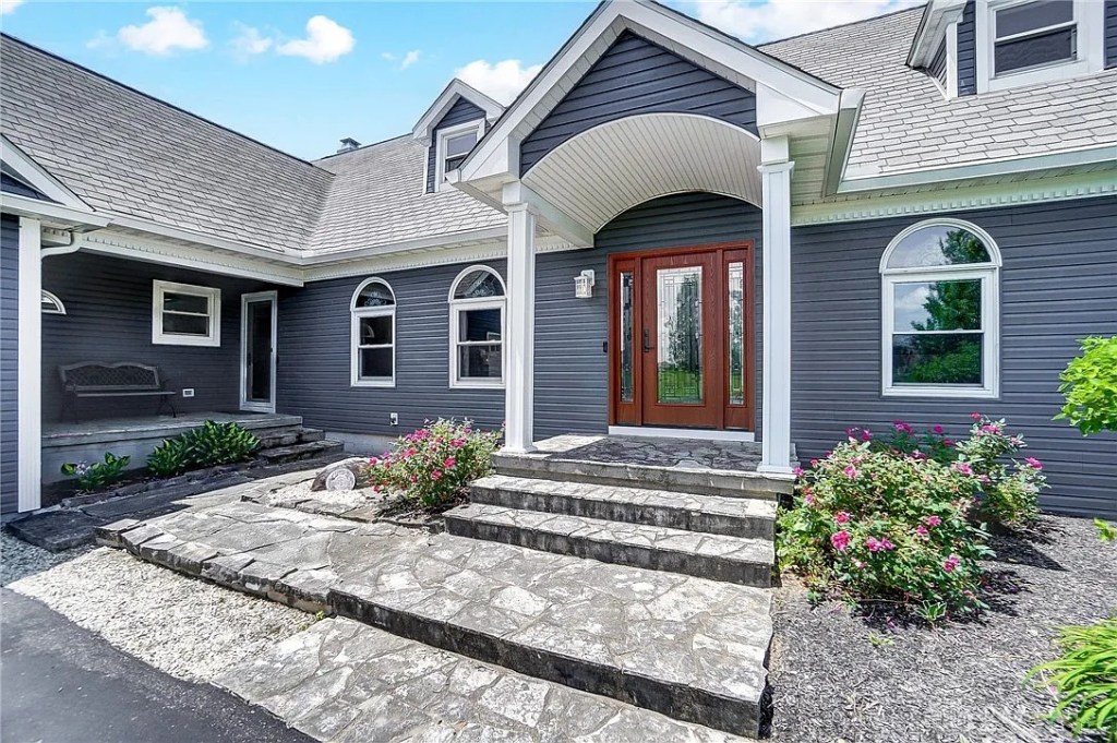 Modern gray home featuring a custom new door with decorative glass inserts, stone walkway, and landscaped entry creating strong curb appeal.