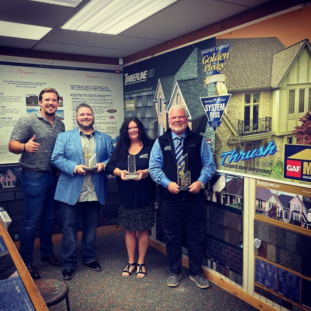 The Thrush family proudly holding GAF Master Elite Roofing Contractor awards inside the Thrush & Son® design center, representing family leadership, trust, and award-winning roofing excellence